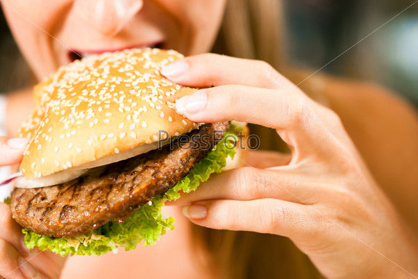 Happy woman in a restaurant eating a fast food hamburger, focus on the burger
