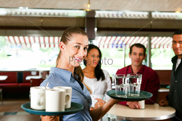Woman as waitress in a bar or restaurant with coffee mugs; in the background are guests, stock photo
