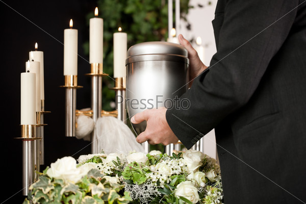 death and dolor  - funeral and cemetery, mortician carrying the urn to a bed of white roses
