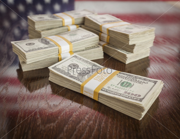 Thousands of Dollars Stacked with Reflection of American Flag on Wooden Table.