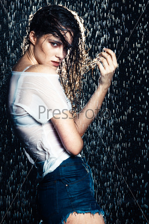 Young beautiful brunette woman posing in wet fashionable clothes and hair, looking at camera.
