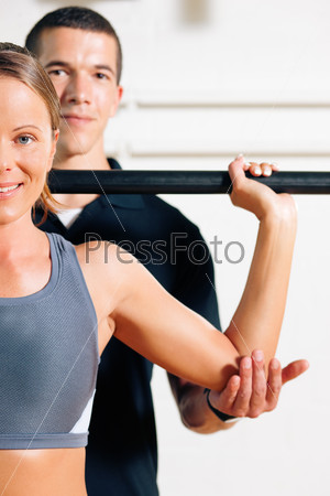 Woman with her personal fitness trainer in the gym exercising power gymnastics with a barbell