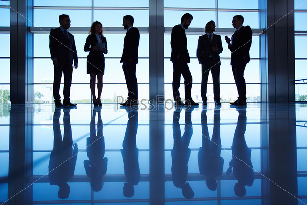 Silhouettes of several office workers standing by the window and working