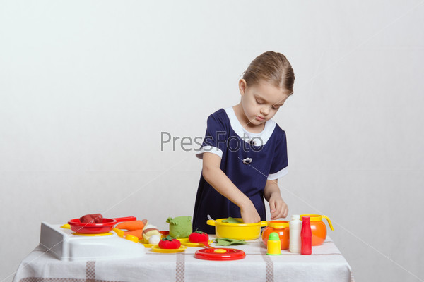 Five year old girl playing in a children\'s mistress dishes at a table covered with a cloth