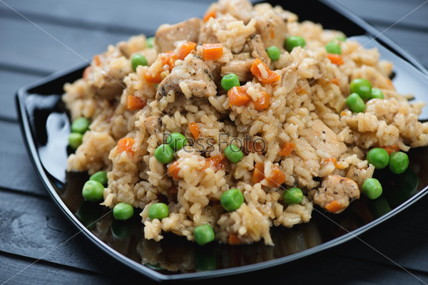 Chicken pilaf with green peas and carrot on a black glass plate
