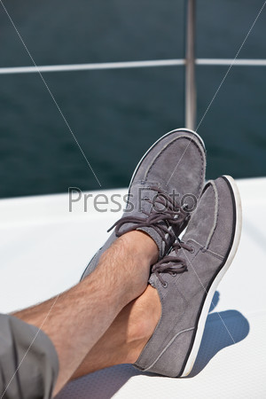 A pair of hairy man legs in pants and topsiders on white yacht deck. Yachting