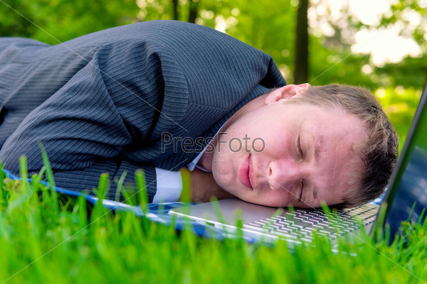 Tired man asleep on a laptop in the park, stock photo
