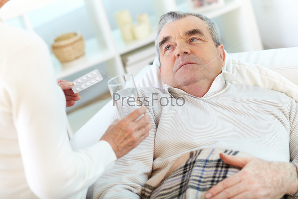Image of sick senior man looking at his wife offering him to take pill