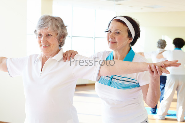 Portrait of sporty female supporting her friend while doing physical exercise in sport gym