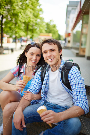 Couple of happy travelers with ice-cream looking at camera during journey