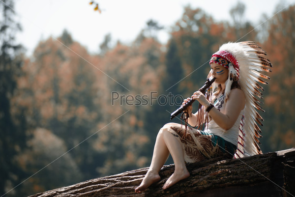 Young woman in war bonnet headdress of American Indian plays on a tree a flute