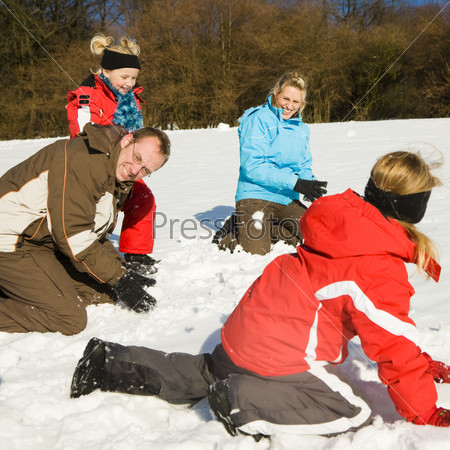 Family with kids having a snowball fight in winter on top of a hill in the snow