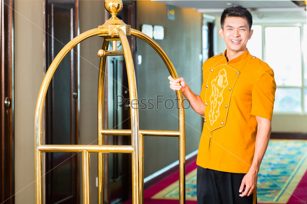 Asian Chinese baggage porter or bell boy or page bringing the suitcase of guests with a box van to the hotel room