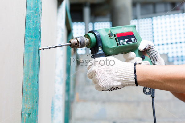 Worker drilling with machine in construction site wall