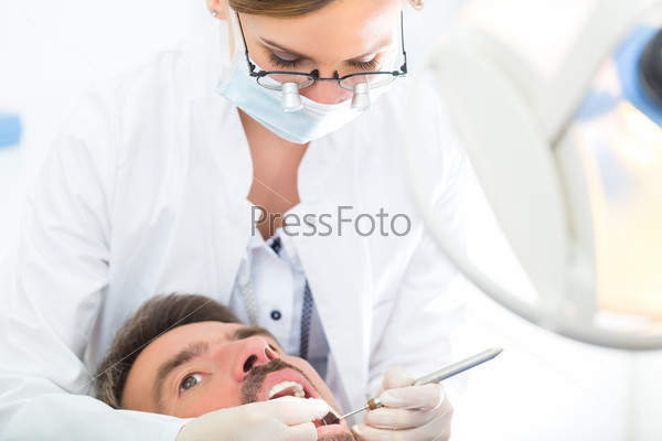 Male patient with female dentist in a dental treatment, wearing masks and gloves