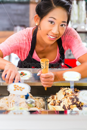 Young Asian saleswoman in an ice cream parlor takes a scoop of ice cream