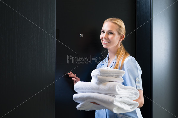 Hotel room service - young chambermaid standing in front of a room door in a suite with fresh towels