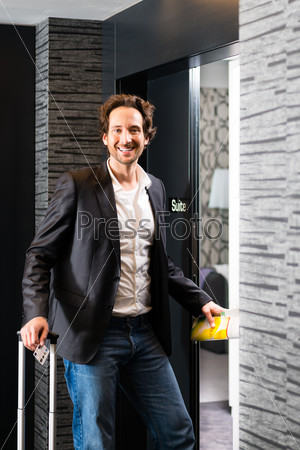 Young man standing with a trolley in front of a room door in a hotel