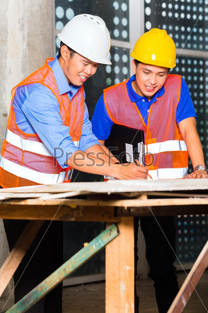 Chinese architect and supervisor point on building site on a construction plan