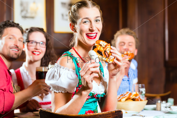 Young people in traditional Bavarian Tracht eating with sausages in restaurant or pub lunch or dinner, stock photo