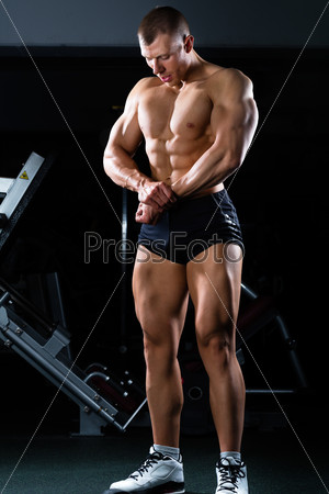 Strong man, bodybuilder posing in Gym, dumbbells are in the background