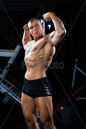 Strong man, bodybuilder posing in Gym, dumbbells are in the background