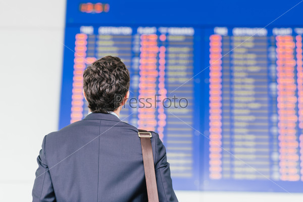 Man looking at the timetable in the airport, view from the back