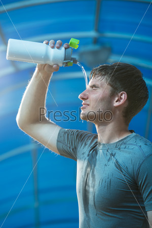Young tired athlete splashing and pouring fresh water on his head to refresh during a running trail