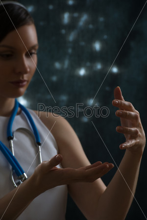 Pretty female doctor with stethoscope wearing futuristic clothes holding something in her hands