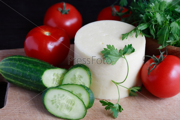 Still life with piece of cheese near various vegetables on cutting board