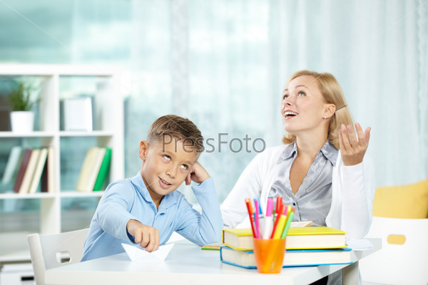 Portrait of handsome boy at workplace with his tutor sitting near by and telling something, stock photo