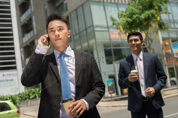 Serious businessman talking on the phone while his colleague waiting for him