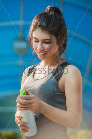 Fitness beautiful woman drinking water and sweating after\
exercising on summer hot day in city. Female athlete after work\
out.