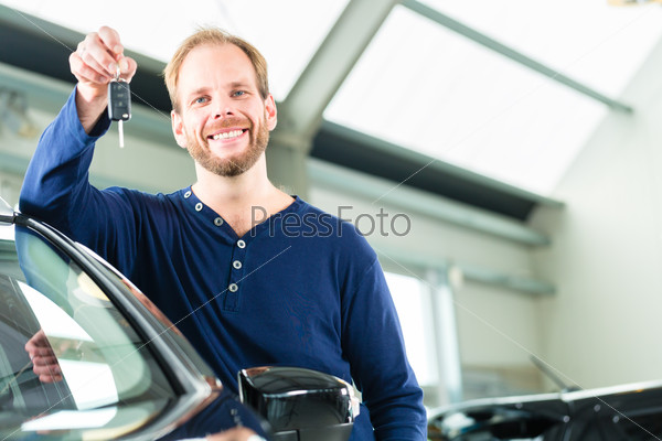 Young man beside a new car in car dealership, obviously he is buying the auto, or making a test drive and holding the keys in hand