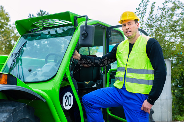 Builder or driver standing in front of construction machinery on building site