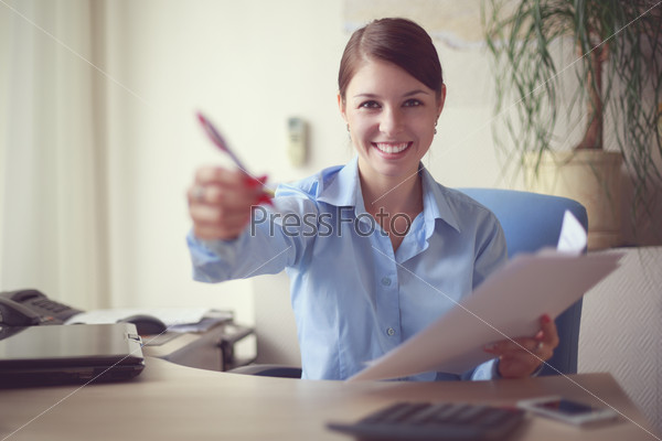 Portrait of young caucasian business woman in blue shirt giving you a pen to document signature.