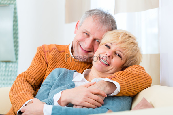 Quality of life - two elderly people sitting at home on the couch, he embraces his wife