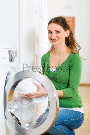 Young woman or housekeeper has laundry day at home, she takes the out of the washing machine or the dryer