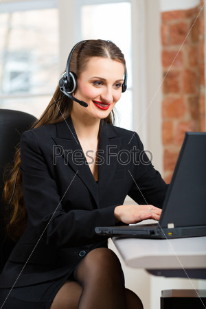 Young businesswoman or secretary working in her Office, she sitting in front of the window and working on a computer with a headset, she has a customer pitch