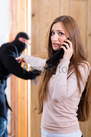 Security - disguised burglar breaking in an apartment or office, a woman calling the police with her phone or telephone