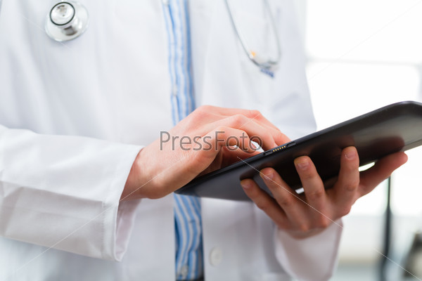 Young doctor standing in clinic reading a file or dossier on the tablet computer