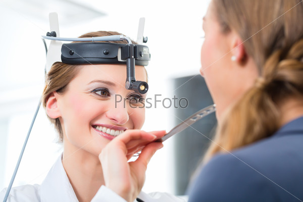 Doctor - Young female doctor or ENT specialist - with a patient in her practice, examining the throat with a spatula