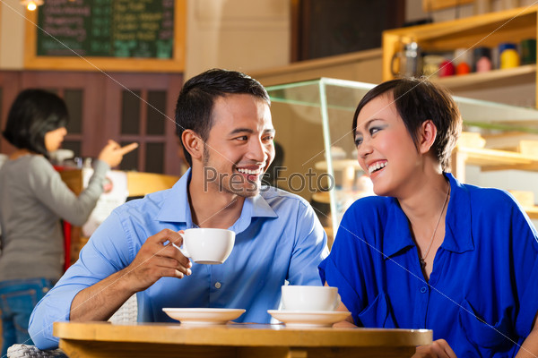 Asian Friends Enjoying Her Leisure Time In A Cafe, Drinking Coffee Or Cappuccino And Talking About Some Things