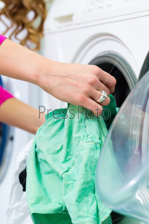 Young woman in a launderette, washing her dirty laundry, in the background are washing machines