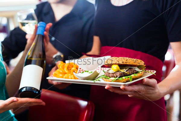 Friends or couple eating fast food in American fast food diner, the waitress serving the food and wine