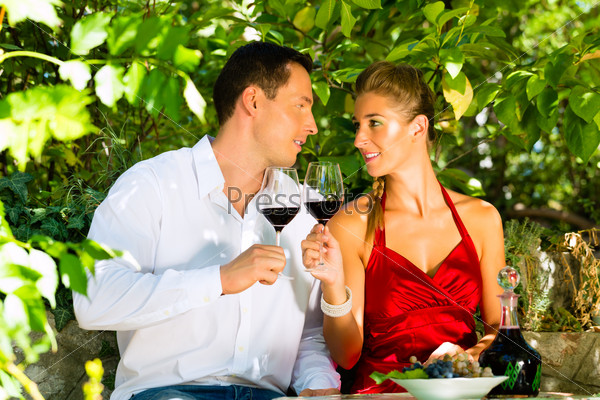 Woman and man sitting romantically under grapevine and drinking wine from a glass