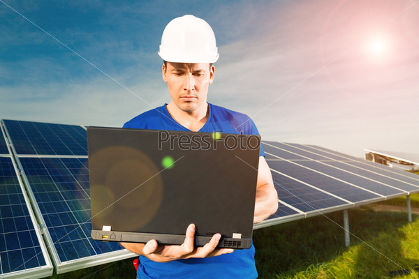 Photovoltaic system with solar panels for the production of renewable energy through solar energy, a technician standing in front with a laptop