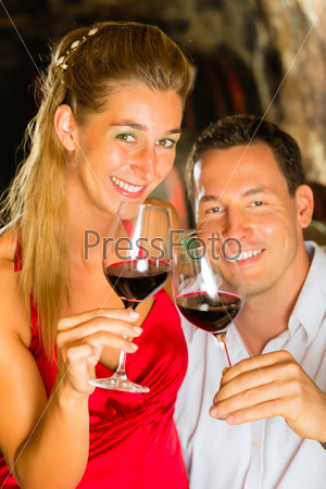 Couple - man and woman- tasting red wine in a cellar, in the background barrels can be seen
