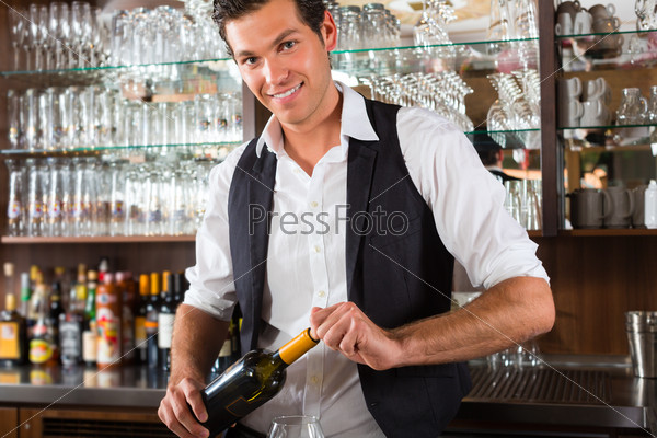 Barman standing behind the bar In restaurant opening a wine bottle