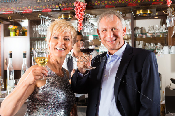 Senior couple in restaurant standing at bar with glass of wine in hand and having fun